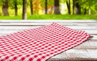 toalha de mesa quadriculada na mesa de madeira no fundo do parque turva foto