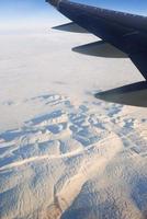 vista para a asa do avião no céu e montanhas nevadas. conceito de viagens e transporte foto