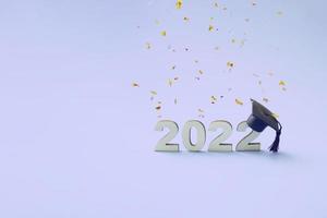 graduação 2022 usando um chapéu de pós-graduação em um número de madeira 2022 em fundo colorido muito rosqueado com confete voador foto