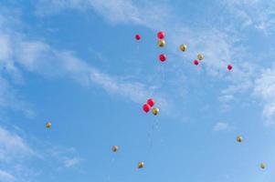 muitos balões vermelhos e dourados voam sob o céu azul e nuvens brancas foto