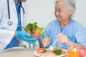 paciente asiático sênior ou idosa idosa comendo alimentos saudáveis de vegetais de café da manhã com esperança e feliz enquanto está sentado e com fome na cama no hospital. foto