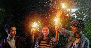 grupo asiático de amigos fazendo churrasco no jardim ao ar livre rindo com bebidas alcoólicas de cerveja e mostrando grupo de amigos se divertindo com estrelinhas na noite foto