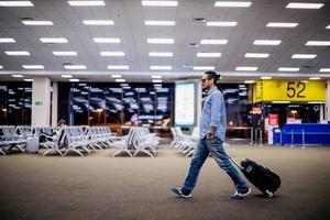 viajante de homem asiático com malas andando e transporte em um aeroporto foto