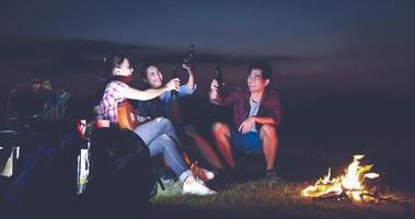 um grupo de turista de amigos asiáticos bebendo e tocando violão junto com a felicidade no verão enquanto acampa perto do lago ao pôr do sol foto