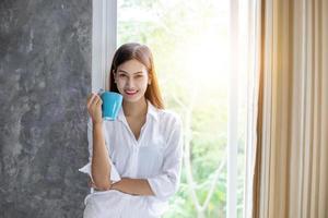 mulheres asiáticas tomando café e acordando em sua cama totalmente descansadas e abrindo as cortinas pela manhã para tomar ar fresco no sol foto