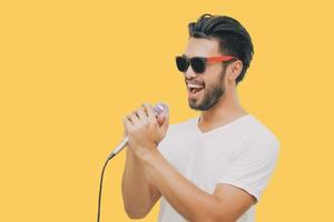 homem bonito asiático com bigode, sorrindo e cantando ao microfone isolado em fundo amarelo foto