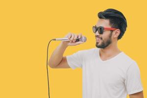 homem bonito asiático com bigode, sorrindo e cantando ao microfone isolado em fundo amarelo foto