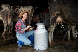 mulheres asiáticas agricultura e indústria agrícola e conceito de pecuária - mulheres jovens ou agricultor com computador tablet pc e vacas em estábulo na fazenda de gado leiteiro com máquinas de ordenha de vaca foto