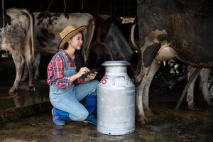 mulheres asiáticas agricultura e indústria agrícola e conceito de pecuária - mulheres jovens ou agricultor com computador tablet pc e vacas em estábulo na fazenda de gado leiteiro com máquinas de ordenha de vaca foto