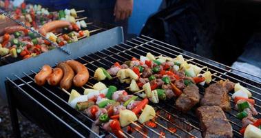 Grupo de amigos asiáticos fazendo churrasco ao ar livre no jardim, rindo com bebidas alcoólicas de cerveja à noite foto