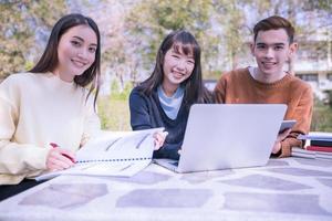 grupo de estudantes universitários asiáticos sentados na grama verde trabalhando e lendo juntos em um parque foto