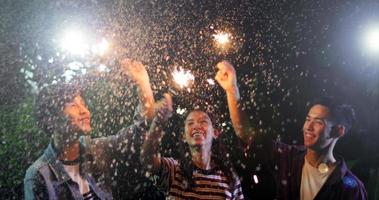 Grupo asiático de amigos fazendo churrasco ao ar livre no jardim, rindo com bebidas alcoólicas de cerveja e mostrando um grupo de amigos se divertindo com estrelinhas à noite, foco suave foto