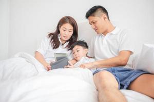 família e filho assistindo e jogando tablet na cama