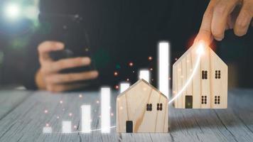 conceito de investimento imobiliário. empresário segurando casas modelo de madeira e gráfico virtual, crescimento imobiliário no futuro, finanças, bancos, empréstimos e comércio. foto