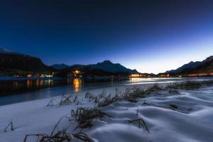 lago alpino à noite com aldeias ao fundo foto