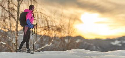 uma garota esportiva observa o pôr do sol durante uma caminhada com raquetes de neve foto