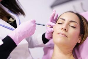 médico injetando ácido hialurônico nas maçãs do rosto de uma mulher como tratamento de rejuvenescimento facial. foto