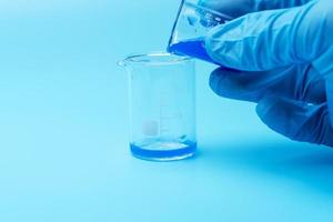 close-up nas mãos de um cientista usando luvas de borracha azul e derramando produtos químicos líquidos de vidro em vidro. foto