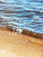 close-up da costa arenosa do lago. espuma na água. areia molhada foto
