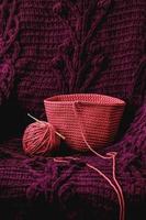 bola de fio rosa com uma agulha e tecido de malha em um fundo de material roxo. copiar, espaço vazio para texto foto