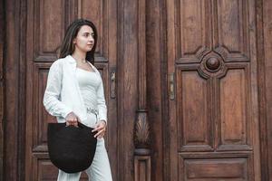 mulher vestindo roupas brancas, segurando o saco de malha no fundo das velhas portas de madeira. copiar, espaço vazio para texto foto