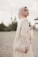 linda modelo feminina islâmica vestindo moda hijab, um vestido de noiva moderno para mulher muçulmana caminha pela areia e pelo mar. um modelo de menina asiática usando hijab se divertindo na praia. foto pré-casamento