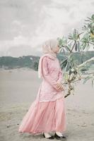 linda modelo feminina islâmica vestindo moda hijab, um vestido de noiva moderno para mulher muçulmana caminha pela areia e pelo mar. um modelo de menina asiática usando hijab se divertindo na praia. foto pré-casamento