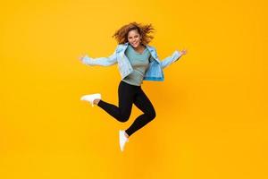 feliz e sorridente jovem afro-americana pulando isolada em fundo amarelo foto