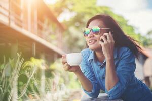 mulher jovem hippie falando telefone enquanto segura uma xícara de café de manhã e sorria. conceito de férias relaxantes. foto