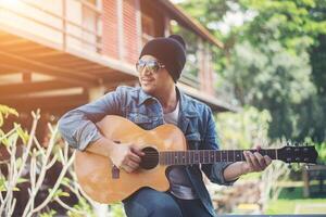 homem hipster sentado enquanto tocava violão e cantava. foto