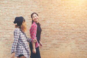 feche o retrato de duas namoradas bonitas e hipster sorriem, divirta-se contra a parede de tijolos urbanos. foto