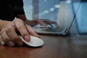 close-up da mão do homem de negócios trabalhando no computador portátil na mesa de madeira foto