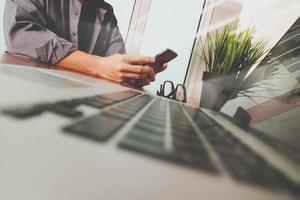 mão de empresário usando telefone celular com computador portátil como conceito de estratégia de negócios foto