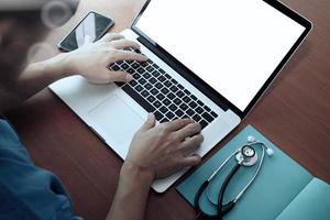 vista superior da mão do médico trabalhando com computador moderno e telefone inteligente na mesa de madeira como conceito médico foto