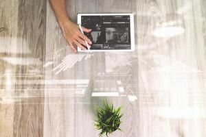 mão de empresário trabalhando com computador tablet digital de caneta stylus. efeito de camada de estratégia de negócios digitais. na mesa de madeira com planta. vista de cima. efeitos de dupla exposição, minimalismo foto