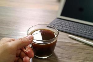 mão segurando a xícara de café ou chá e teclado inteligente dock de mesa digital, caneta stylus na mesa de madeira, efeito de filtro foto