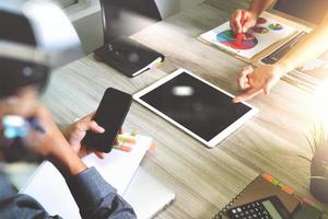 documentos de negócios na mesa de escritório com telefone inteligente e computador portátil e negócios gráficos com diagrama de rede social e três colegas discutindo dados em segundo plano foto