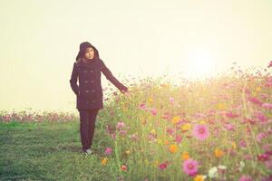 mulher bonita vestindo um casaco preto andando no jardim de flores tempo feliz no inverno foto