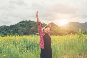 jovem mulher feliz levantando as mãos no campo de flores amarelas no pôr do sol, fundo de vista para a montanha. foto