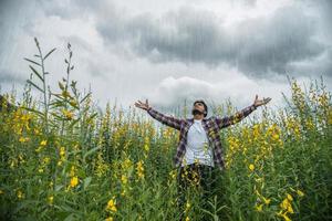 homem bonito hipster em pé levantando as mãos no ar em um campo de flores amarelas. foto