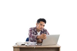 pensativo jovem olhando para laptop enquanto está sentado em seu local de trabalho isolado no fundo branco. foto