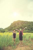 mulher de dois hipster viajando e levantando as mãos desfrutando com campo de flores juntos, relaxante bom tempo dia ensolarado. foto