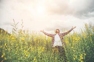 homem bonito hipster em pé levantando as mãos no ar em um campo de flores amarelas. foto