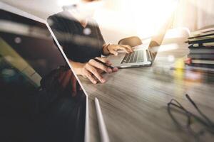 mão de designer trabalhando com tablet digital e computador portátil e pilha de livros e óculos na mesa de madeira como conceito foto