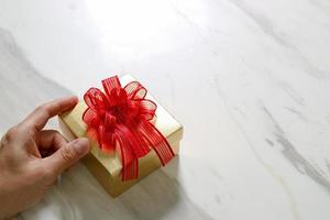 presentear, mão de homem segurando uma caixa de presente em um gesto de dar no fundo da mesa de mármore cinza branco foto