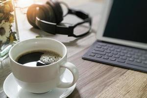 xícara de café e teclado inteligente dock de mesa digital, ervas de flores de vaso, fone de ouvido de música, óculos na mesa de madeira, efeito de filtro foto