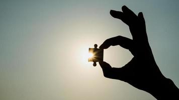 closeup de silhueta da mão segurando um pedaço de quebra-cabeça sobre o efeito da luz solar. símbolo do conceito de associação e conexão. estratégia de negócio. foto