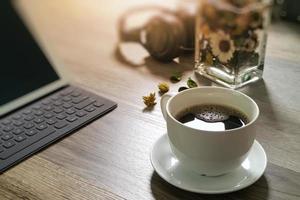 xícara de café e teclado inteligente dock de mesa digital, ervas de flores de vaso, fone de ouvido de música, óculos na mesa de madeira, efeito de filtro foto