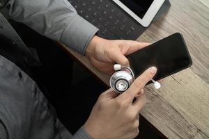 vista superior da mão do médico trabalhando com telefone inteligente, computador tablet digital, óculos estetoscópio, na mesa de madeira foto