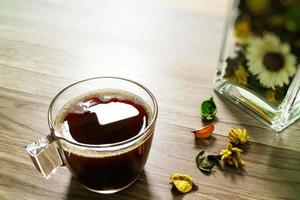 xícara de café ou chá, ervas de flores secas de vaso de vidro, na mesa de madeira, efeito de filtro, close-up foto